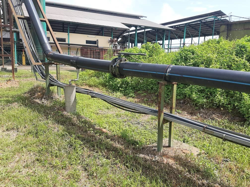 Black pipeline with a flanged joint on steel supports at a palm oil site